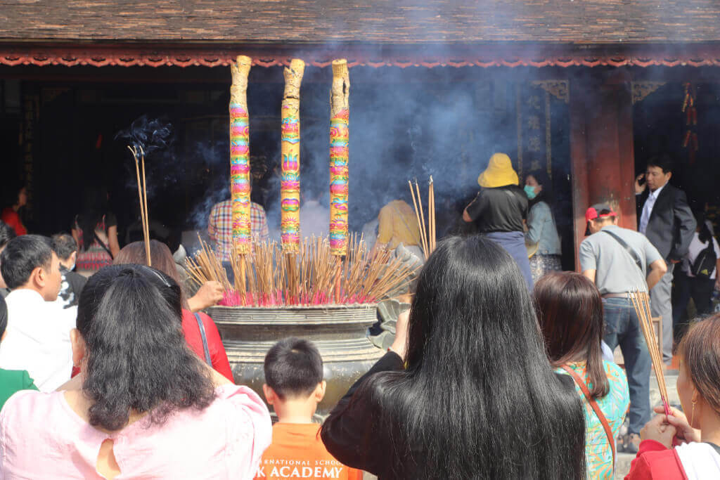 Rückansicht von betenden Menschen vor einem großem Räucherstäbchenbehälter im Innenhof einer vietnamesischen Pagode 