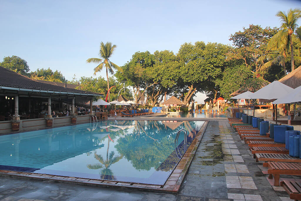 Hotelanlage mit großem Pool, Palmen und Sonnenliegen auf Bali.