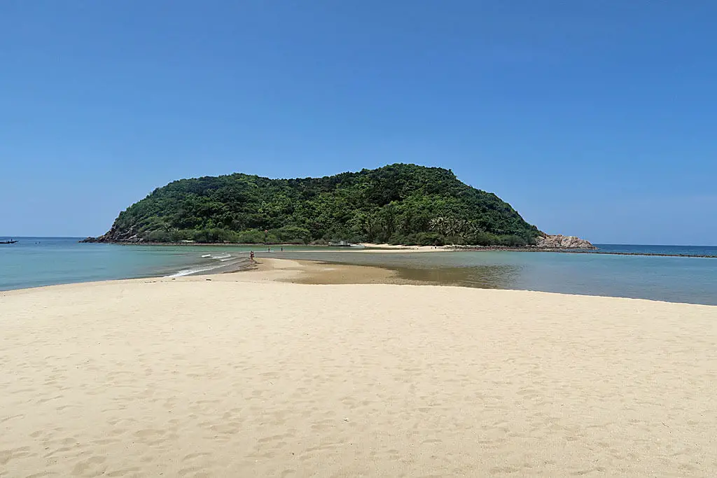 Über eine breite Sandbank laufen Menschen bis zur vorgelagerten Insel