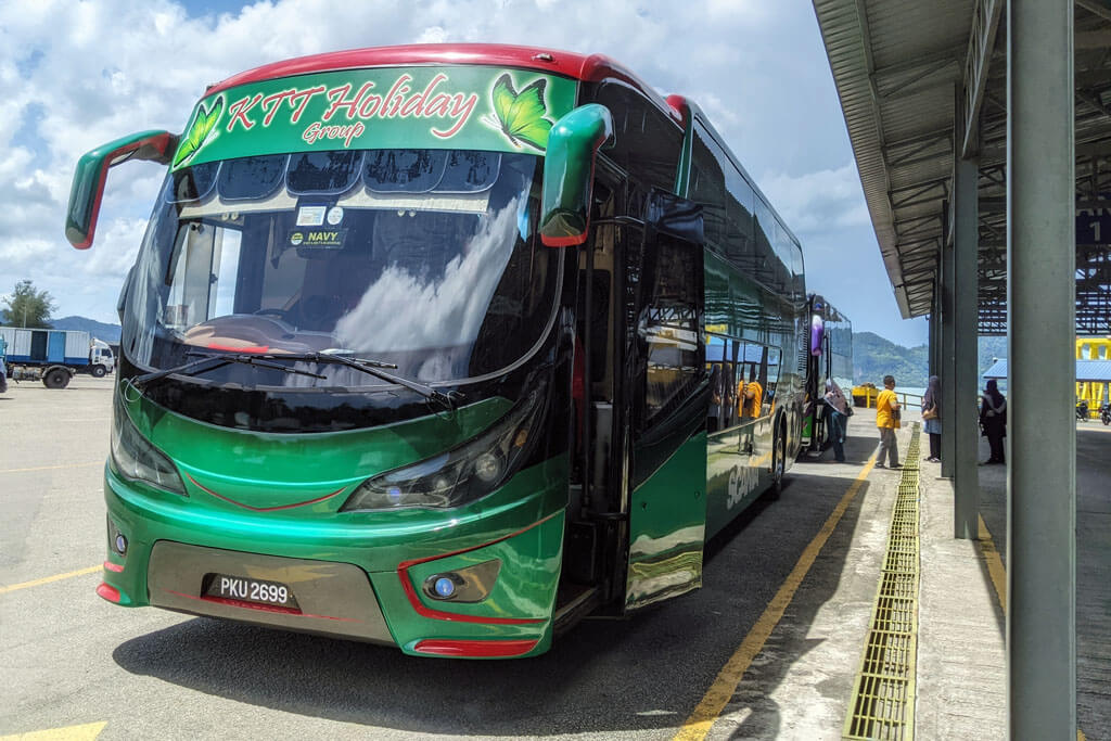 Großer grüner Reisebus mit offener Tür steht am Busterminal mit Meer im Hintergrund in Malaysia