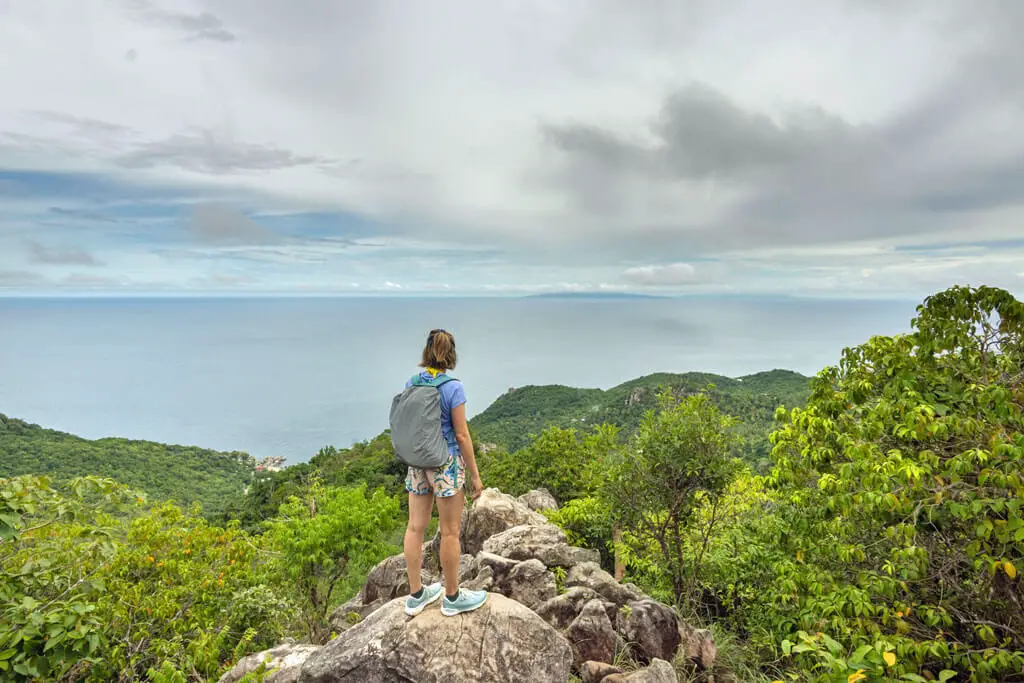 Frau mit Rucksack steht auf einem Felsen an einem Viewpoint in Koh Tao und schaut aufs Meer