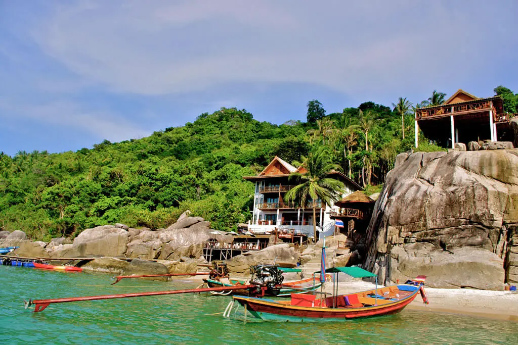 Longtail-Boot vor Felsen und Bungalows in einer Bucht in Koh Tao