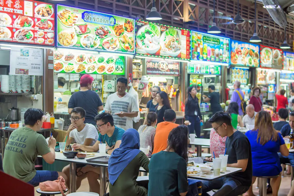 Belebtes Hawker-Center in Singapur mit verschiedenen Ständen und Tischen, an denen Leute essen