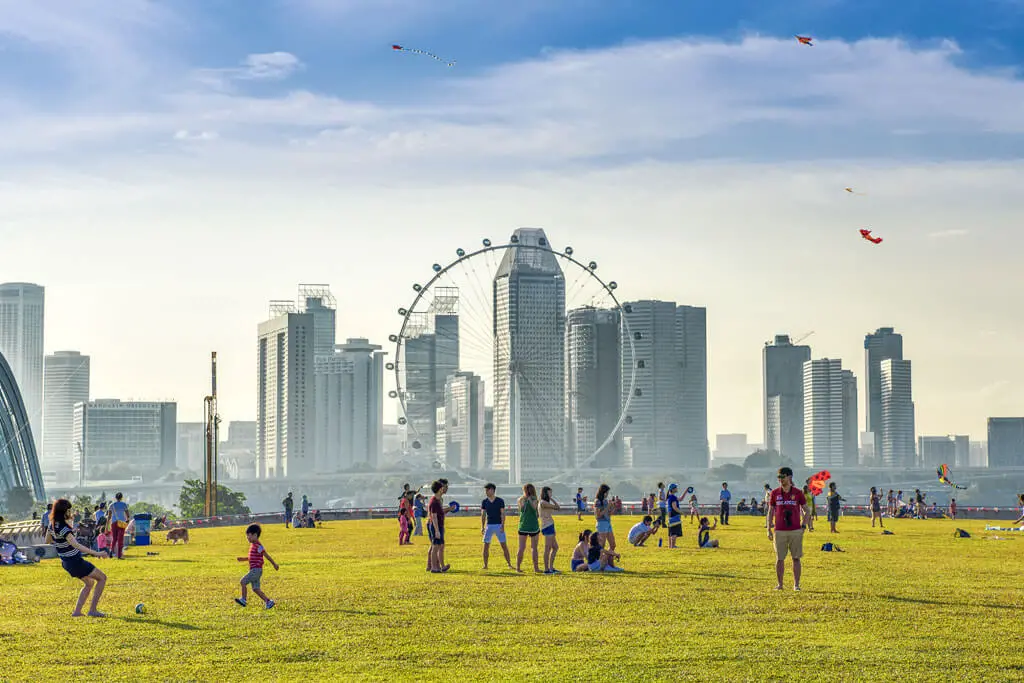 Spielende Kinder auf einem Rasen vor der Skyline von Singapur und dem Singapore Flyer