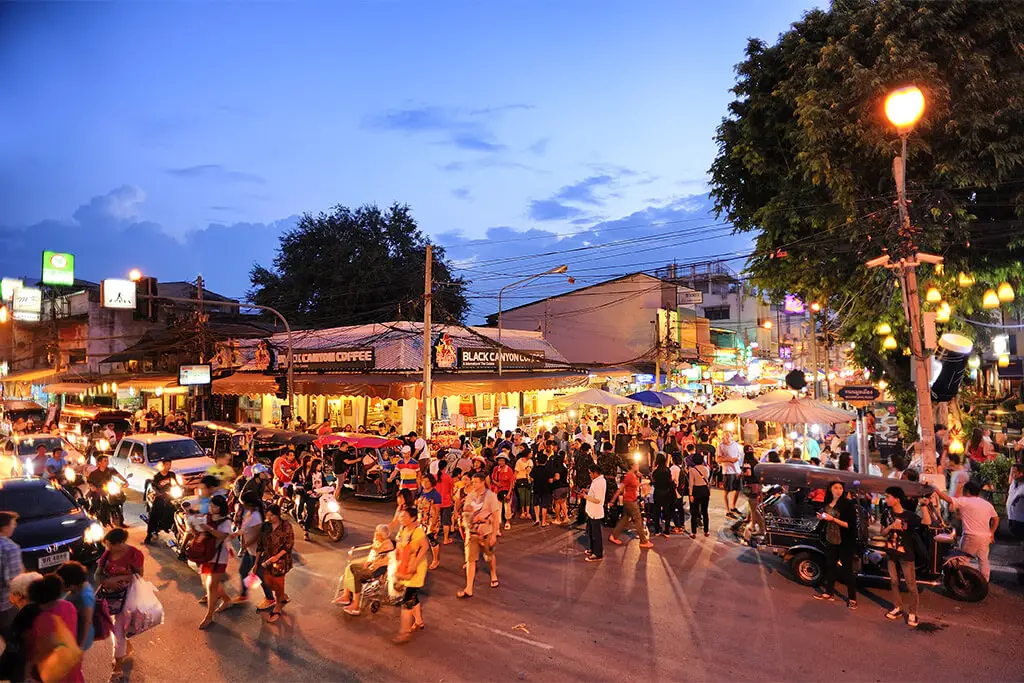 Wuselige Straßenkreuzung in der Altstadt von Chiang Mai am frühen Abend mit Autos und Passanten