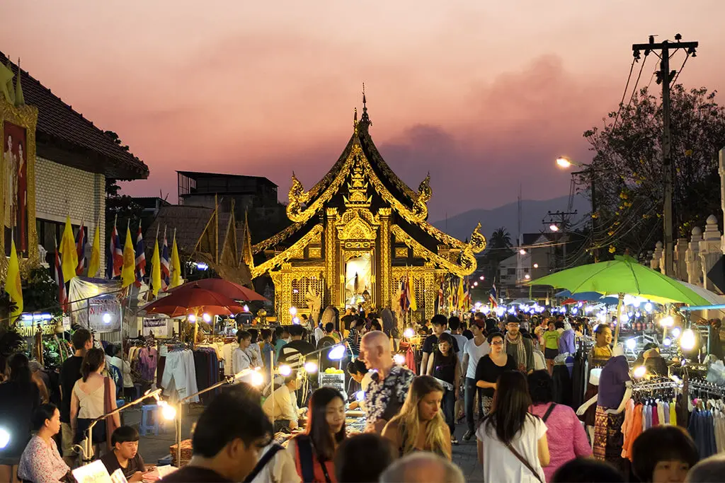 Stände und Personen in der Sunday Walking Street mit goldenem Tempel zur Abenddämmerung