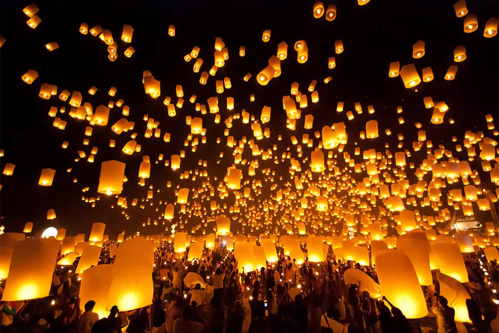 Menschen die tausende von Lampions in den schwarzen Himmel aufsteigen lassen während Yi Peng in Chiang Mai