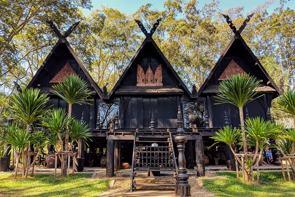 Schwarze Häuser umgeben von grünen Bäumen, die zum Baan Dam Museum in Chiang Rai gehören