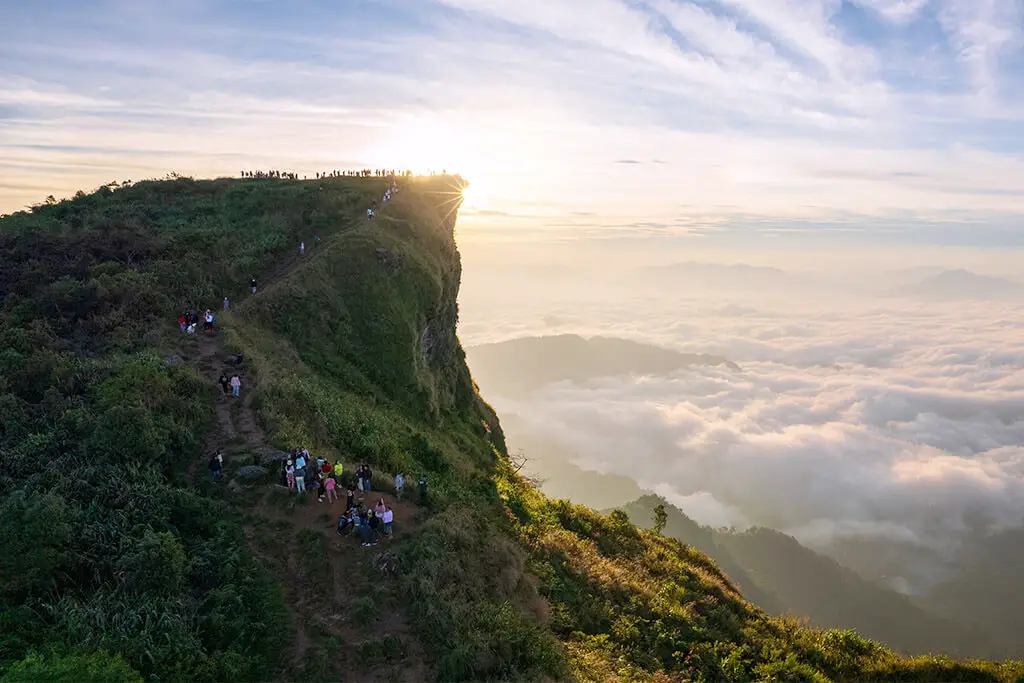 Grüner Gipfel des Phu Chi Fa zum Sonnenaufgang über den Wolken mit Wanderern