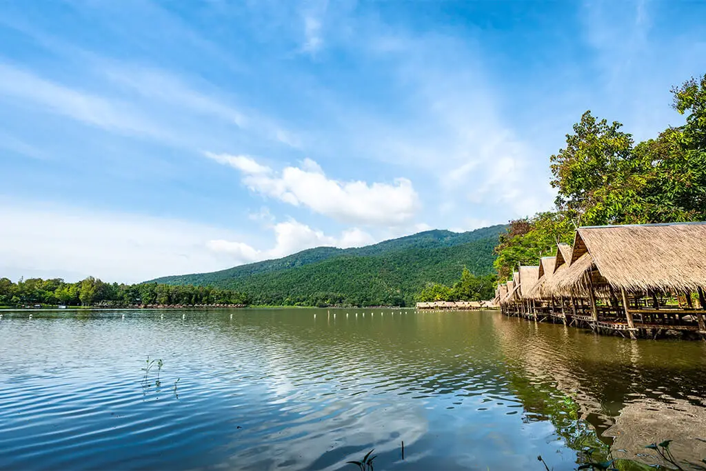 Hütten am Ufer des Huay Tung Tao Sees mit grünen Bergen im Hintergrund