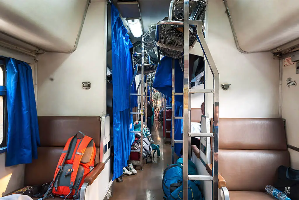 Thailändischer Zug mit Rucksäcken auf den Sitzen und blauen Vorhängen