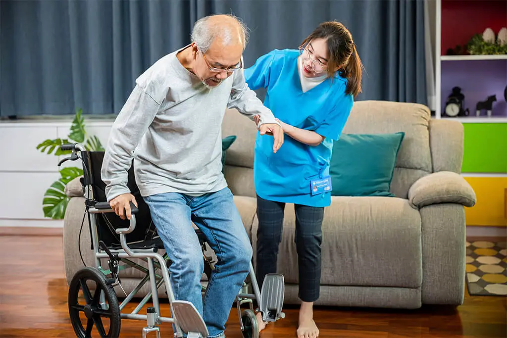 Pflegerin hilft Mann aus dem Rollstuhl