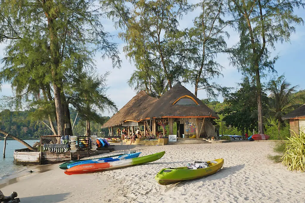 Zwei Kajaks liegen am Strand vor Bäumen und einer Hotelanlage