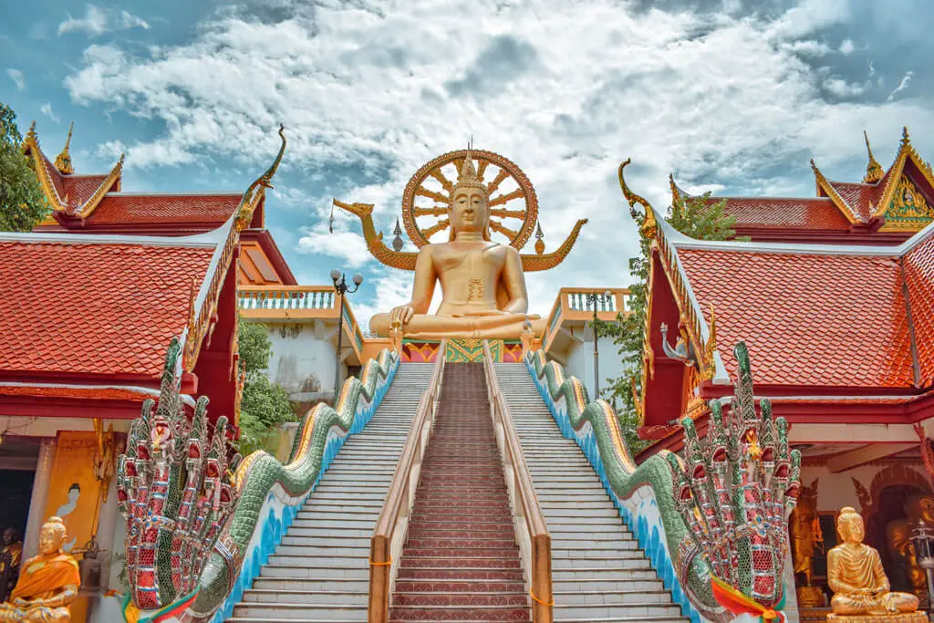 Eine Treppe führt hinauf zu einer goldenen Buddha-Figur im Schneidersitz