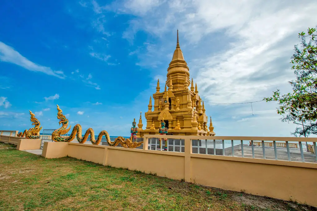 Eine goldene Stupa mit vielen kleinen Türmchen thront hinter einer Mauer direkt am Strand