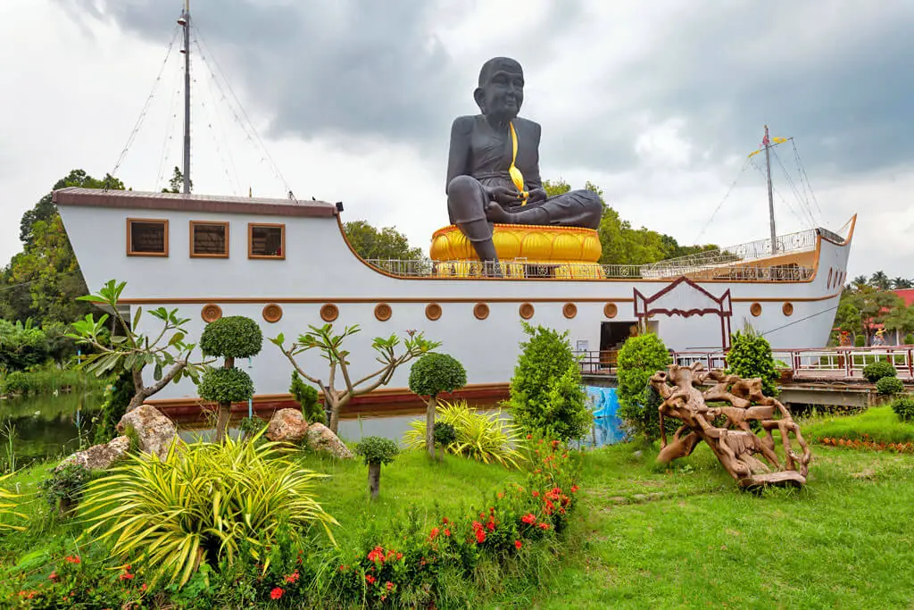 Eine schwarze Mönchs-Statue sitzt auf einem weißen Schiff in einem Garten