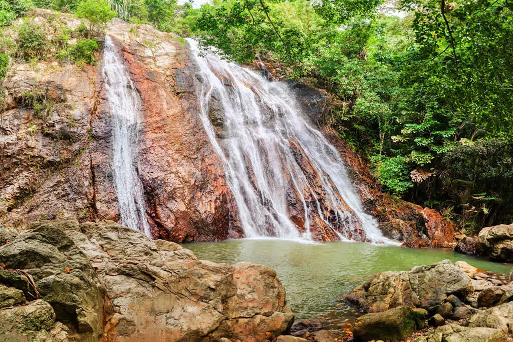 Ein Wasserfall fließt große Felsen hinab, ringsum wuchert der Dschungel