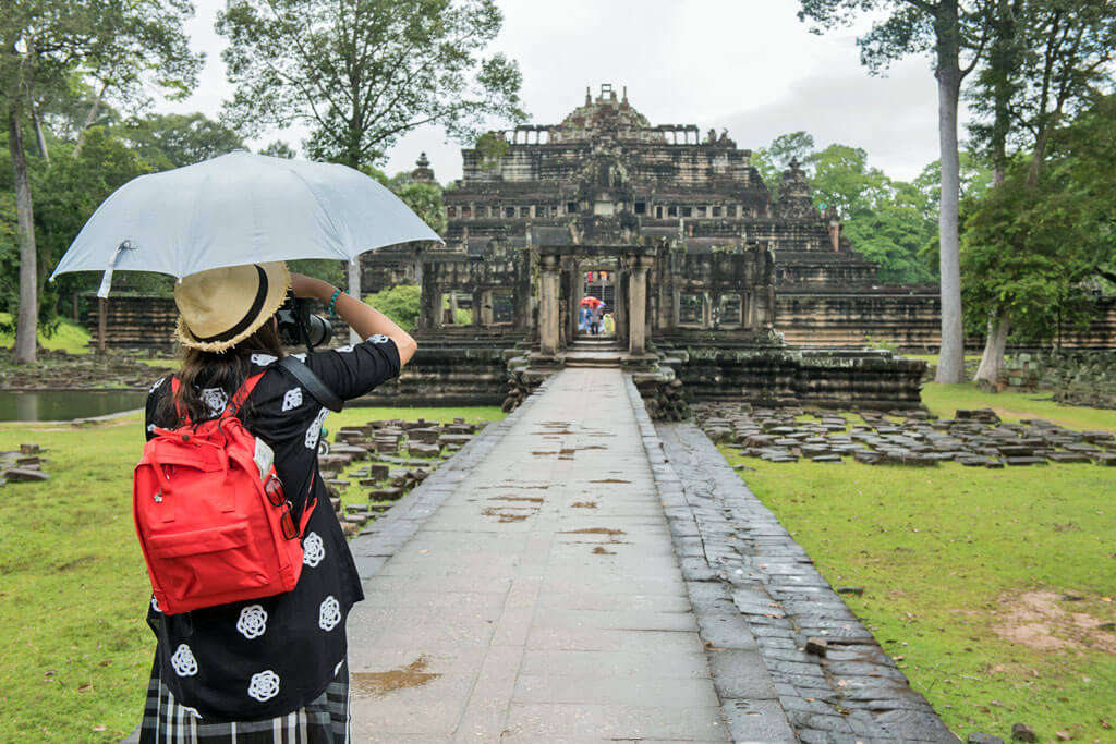 Frau mit Regenschirm fotografiert Angkor Tempel im Regen