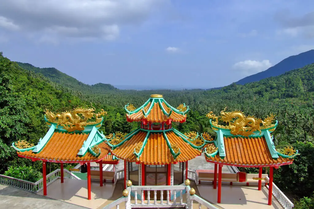 Ein chinesischer Tempel mit drei verzierten Dächern, dahinter weiter Dschungel