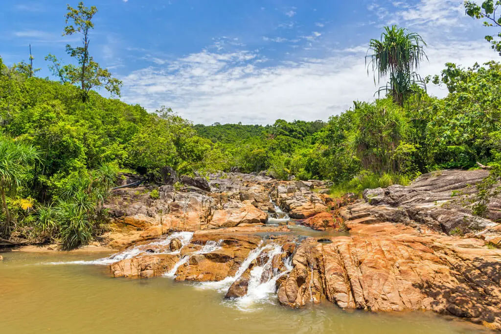 Ein Wasserfall schlängelt sich über ein breites Flussbett aus Felsen, links und rechts Dschungel