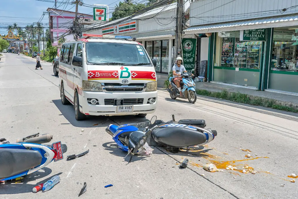 Zwei Roller liegen nach einem Unfall auf einer Straße, ein Krankenwagen steht parat