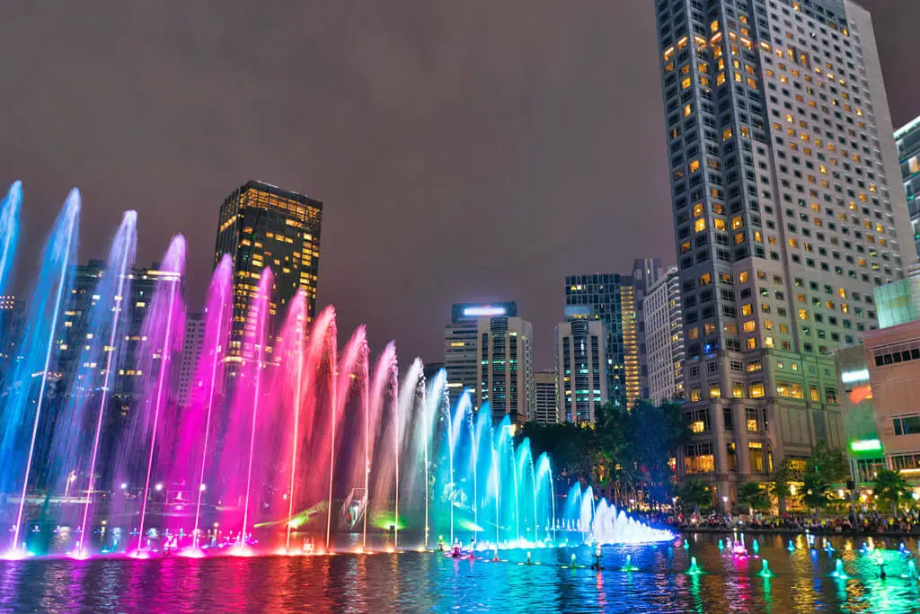 Wasserfontänen in verschiedenfarbiger Beleuchtung vor der Skyline Kuala Lumpurs