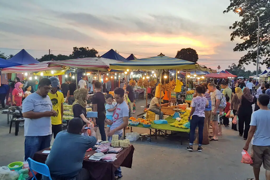 Ein Nachtmarkt bei Sonnenuntergang mit bunten Pavillions und vielen Garküchen sowie Menschen