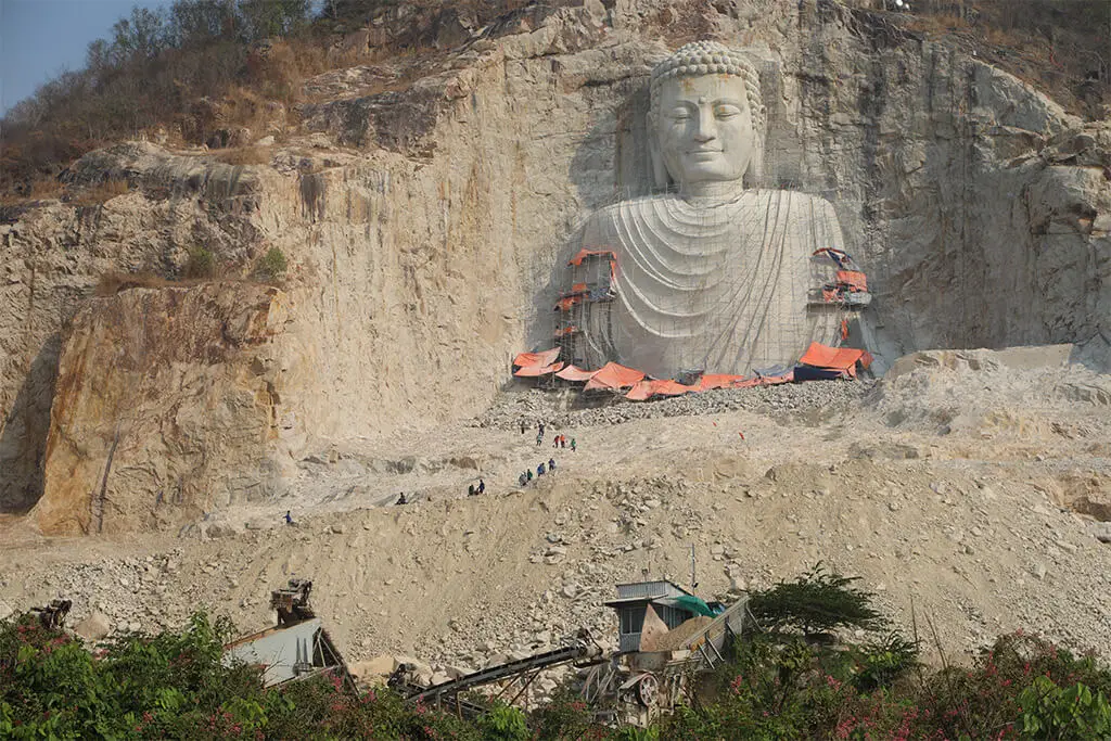 Berghang mit Baustelle von halb fertiggestellter sehr großer Buddhastatue, die aus dem Felsen gearbeitet wird