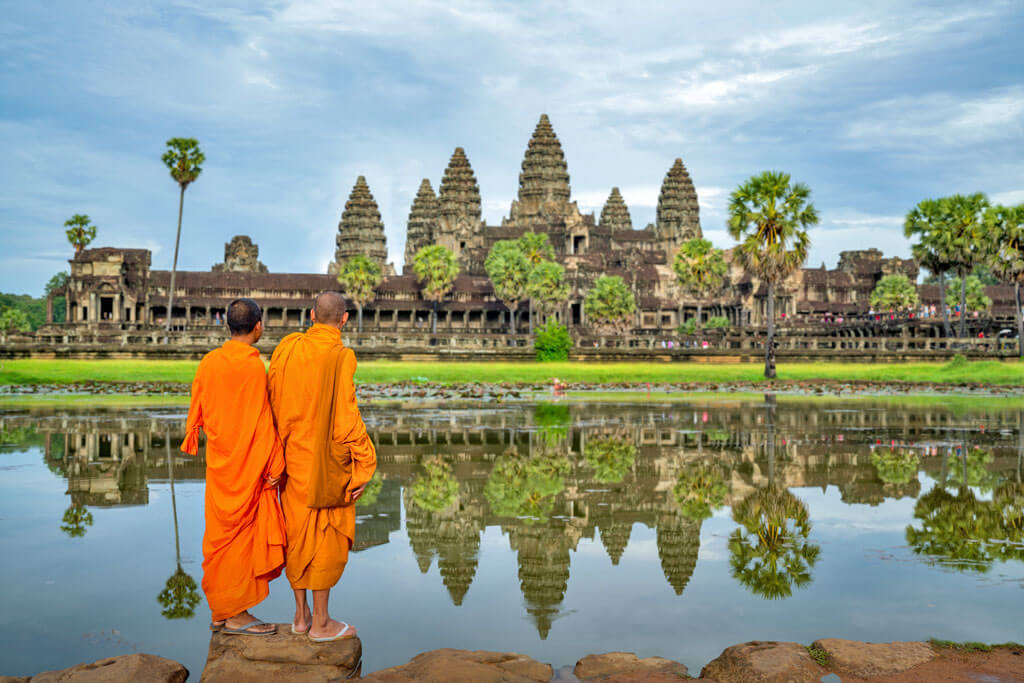 Zwei Mönche in orangener Robe stehen vor der großen Tempelanlage Angkor Wat