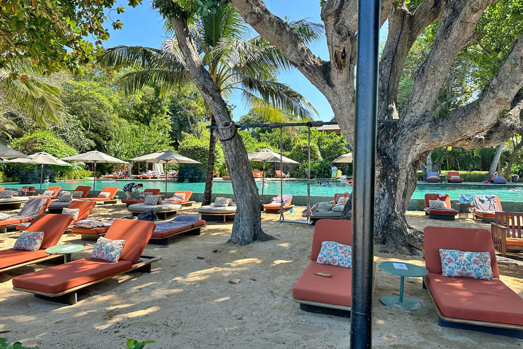 Orangene Hotelliegen im Sand von Sanur, dahinter ist ein breiter Pool