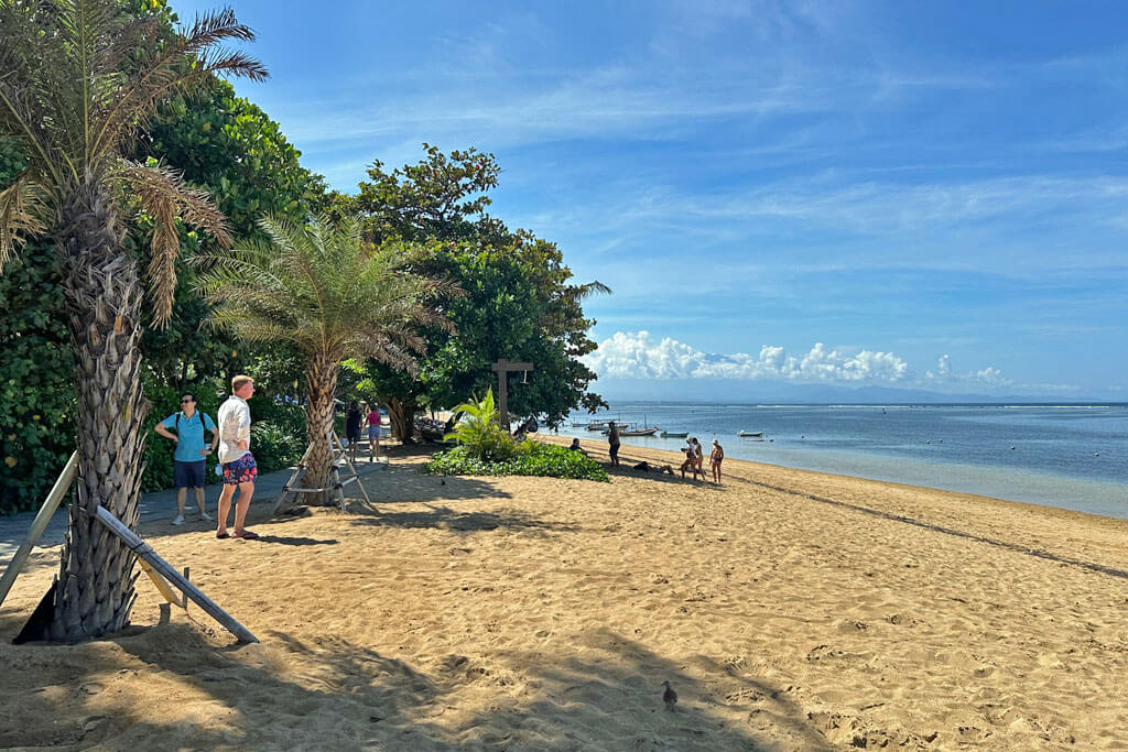 Goldgelber Sand mit Palmen und klares Meer am Strand von Sanur auf Bali