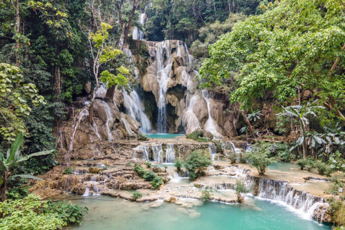 Ein Wasserfall fällt hinab über Felsen hinein in mehrere Pools. Rundum dichter Dschungel