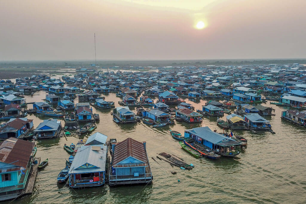 Vogelperspektive auf Häuser eines schwimmenden Dorfes und Boote auf dem Wasser zum Sonnenuntergang