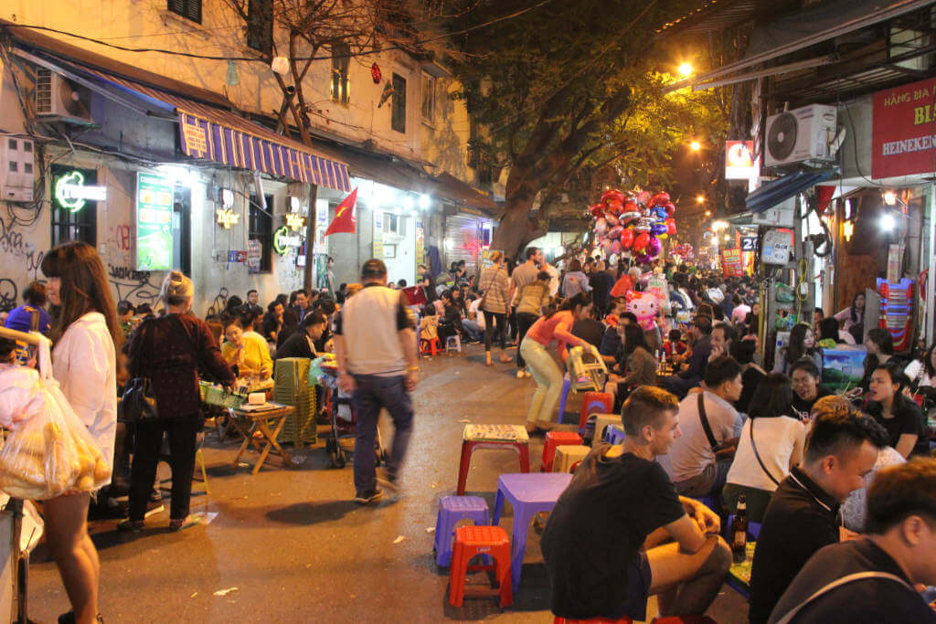 Hanoi bei Nacht, (c) Mark Markand Nachtaufnahme einer belebten Straße mit Bars und niedrigen Plastikmöbeln in der Altstadt von Hanoi
