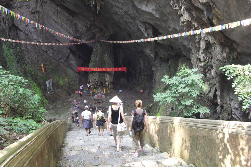 Eine steile Treppe, auf der einige Menschen in Rückansicht zu sehen sind, führt zum Eingang einer Grotte, in der sich ein buddhistisches Heiligtum befindet.