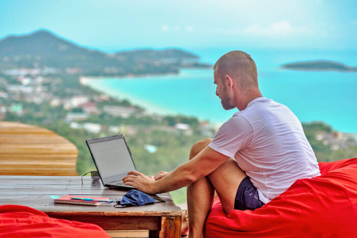 Ein Mann sitzt mit Laptop in einem Sitzsack in einem Restaurant mit Ausblick auf eine Insel