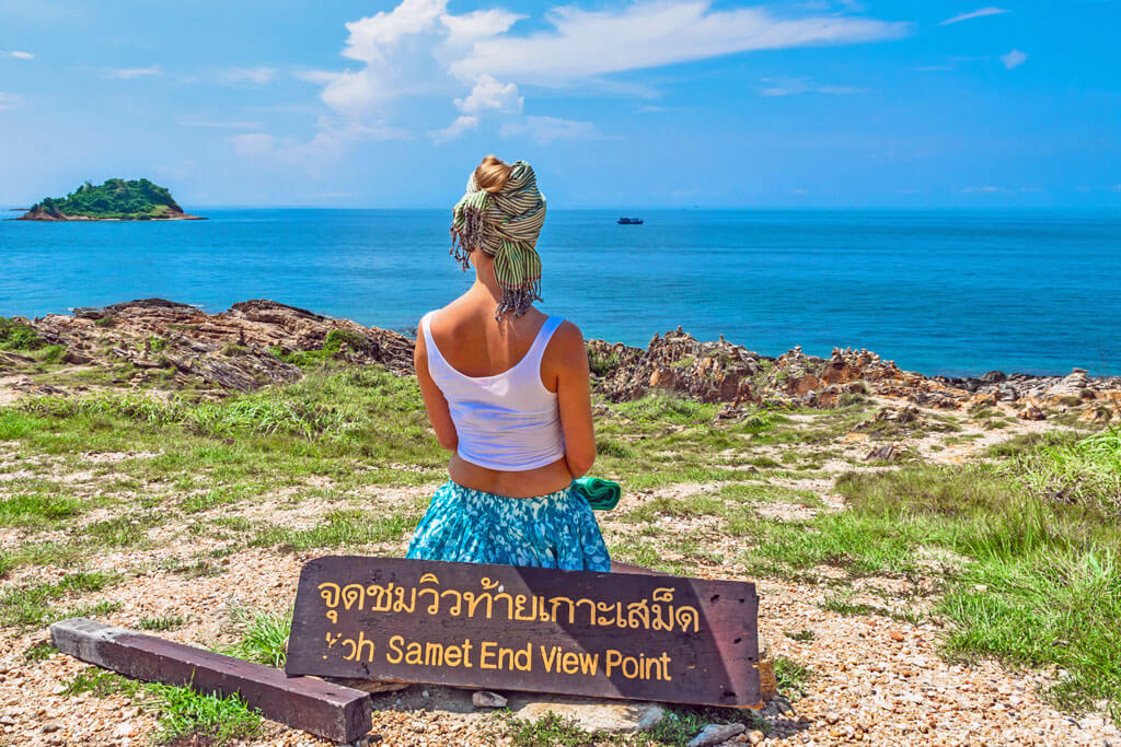 Eine Frau steht an einem Aussichtspunkt mit vielen Steinen und Felsen und schaut aufs Meer