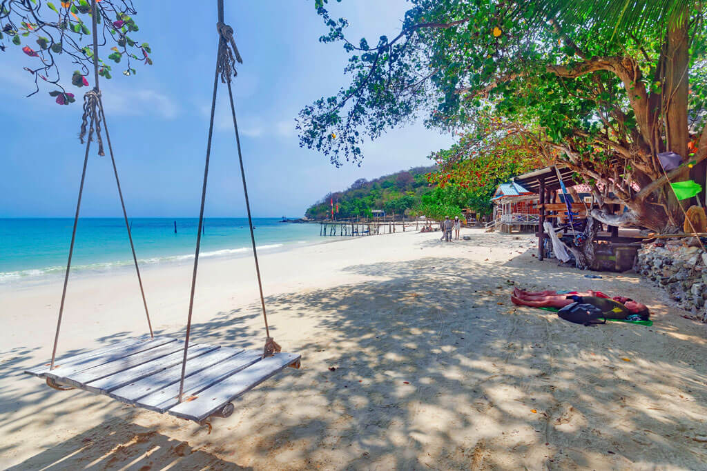 Eine Schaukel am Meer mit weißem Sand und vielen Bäumen