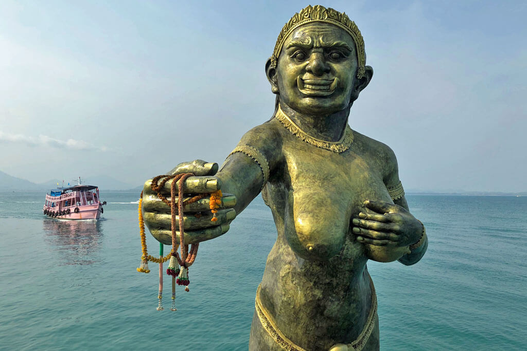 Eine Statue eines weiblichen Ogers steht im Meer und hält Blumengirlanden in der Hand