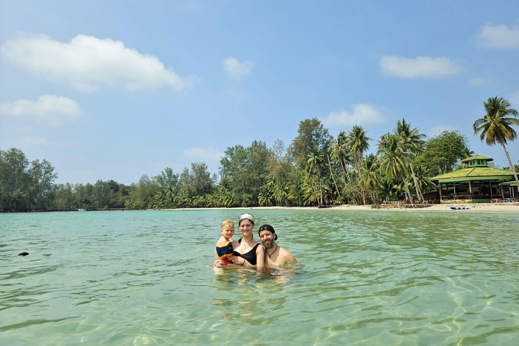 Eine Familie mit Kleinkind im Meer, dahinter Palmen und ein Strand
