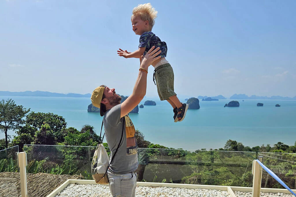 Ein Mann wirft ein Kleinkind in die Luft, im Hintergrund kleine Inseln im Meer