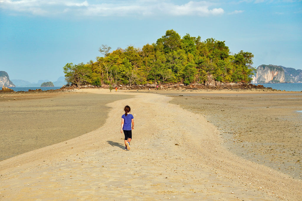 Ein kleines Mädchen läuft auf einer Sandbank auf eine Insel zu