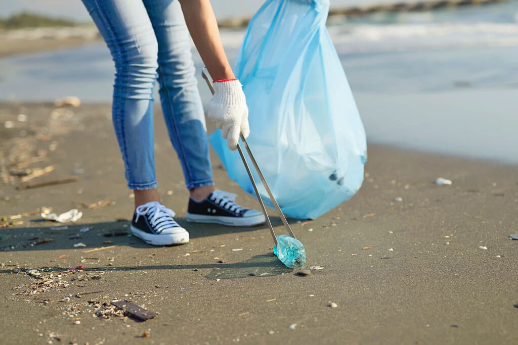 Am Strand wird Müll aufgesammelt und in einen Müllbeutel getan