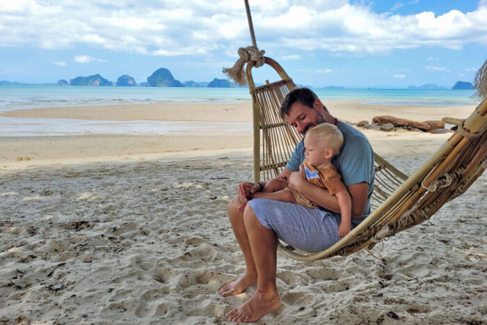 Ein Mann mit einem Baby auf einer Holz-Hängematte am Strand
