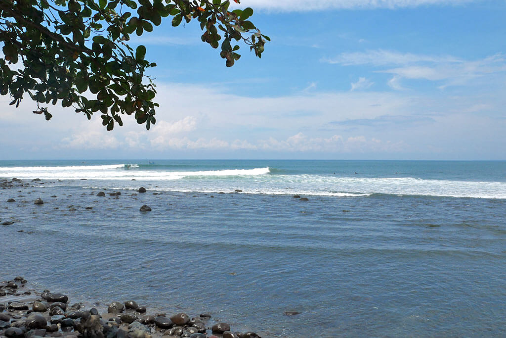 Ruhige Bucht mit schwarzen Steinen am Medewi Beach mit blauem Himmel im Hintergrund