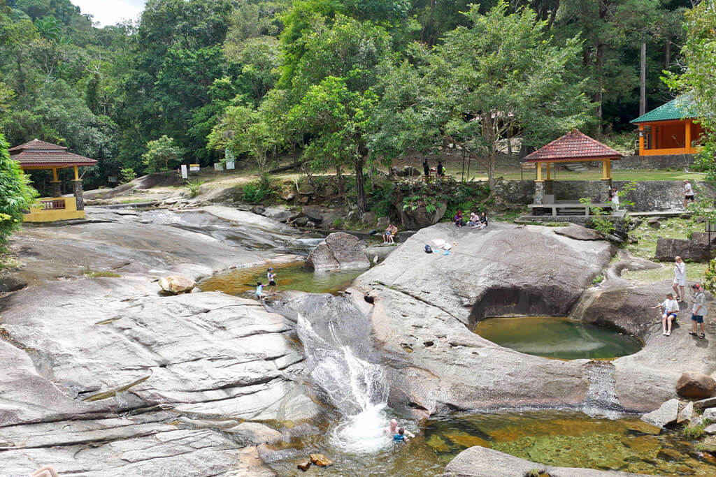 Touristen baden in den natürlichen Badepools am Wasserfall auf Langkawi, Malaysia