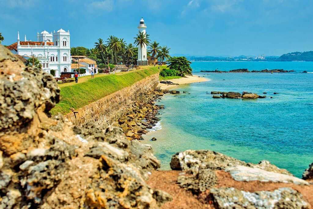 Blick auf die Küste mit einem Leuchtturm, einer Mauer und Palmen