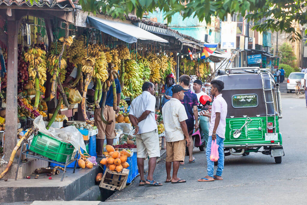 Ein Markt an einer Straße mit vielen Bananen, Tuk Tuks und Menschen