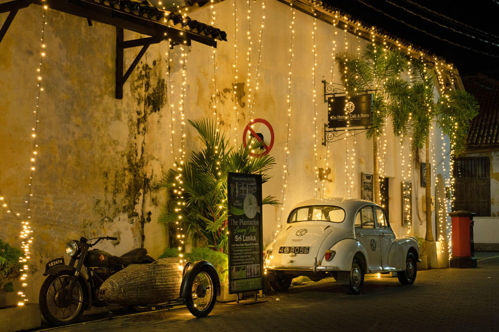 Ein Oldtimer und ein altes Motorrad an einer Wand mir Lichterketten bei Nacht