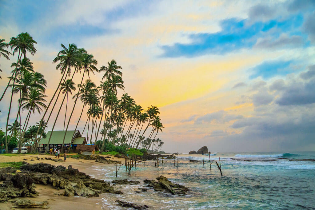 Ein Haus am Strand mit Palmen direkt am Meer bei Sonnenuntergang